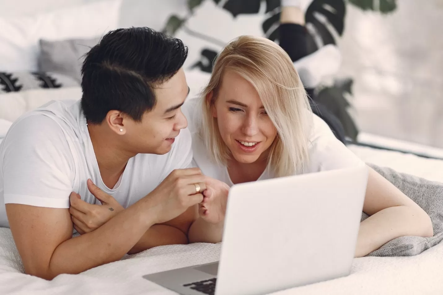 Asian male and blonde female in white t shirts using laptop together